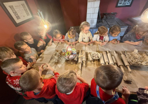 dzieci siedzą przy długim stole prostokątnym i pracują w glinie, używają wałków