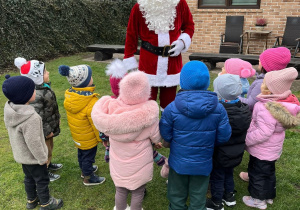 dzieci stoją przed Mikołajem, który rozdaje prezenty