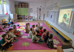 dzieci siedzą na dywanie i na tablicy interaktywnej oglądają film o górnictwie