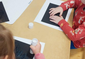 dzieci siedzą przy stolikach i tworzą czapki górnicze z papieru