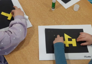 dzieci siedzą przy stolikach i tworzą czapki górnicze z papieru