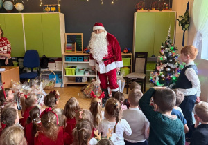 Dzieci siedzą przed świętym Mikołajem w oczekiwaniu na prezenty