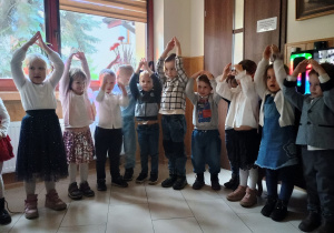 Dzieci w galowych strojach stoją w półkolu świetlicy Domu Akacja, śpiewają piosenki patriotyczne