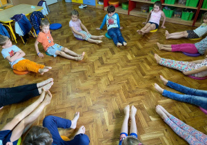 Dzieci siedzą w kółku ćwiczą paluszki u stóp