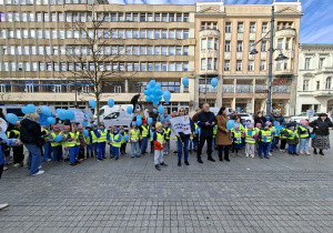 Tłum dzieci ubrany w żółte kamizelki stoi na Pasażu Schillera trzymając niebieskie balony. Z przodu grupy dzieci stoi pani wiceprezydent oraz pan wicekurator oświaty
