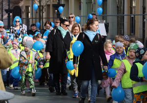 Tłum dzieci z niebieskimi balonami idzie ulicą Piotrkowską wraz z nauczycielami i opiekunami